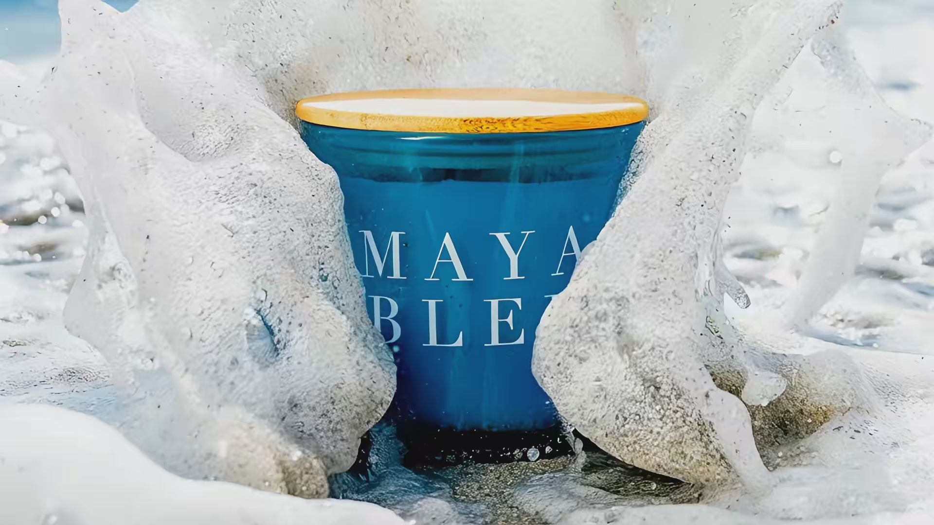 eco friendly soy candle created by Maya Bleu being engulfed by a wave on the beach